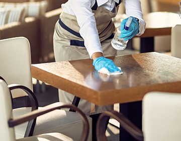 Young waitress disinfecting tables while wearing protective face mask ad gloves due to coronavirus epidemic.